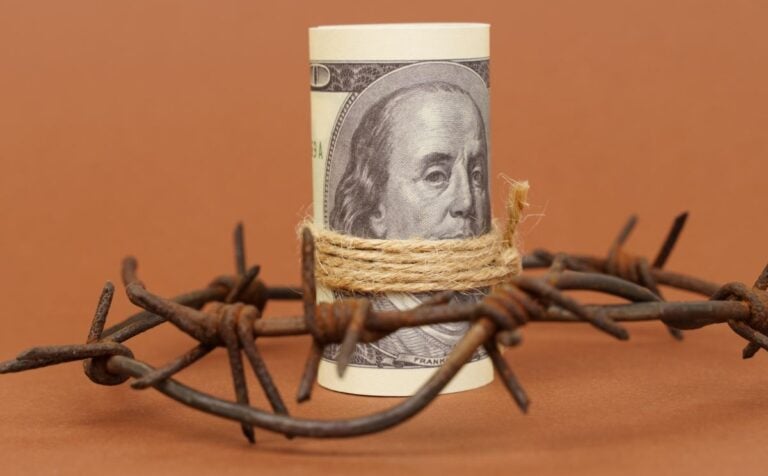 roll of dollar bills surrounded by barbed wire