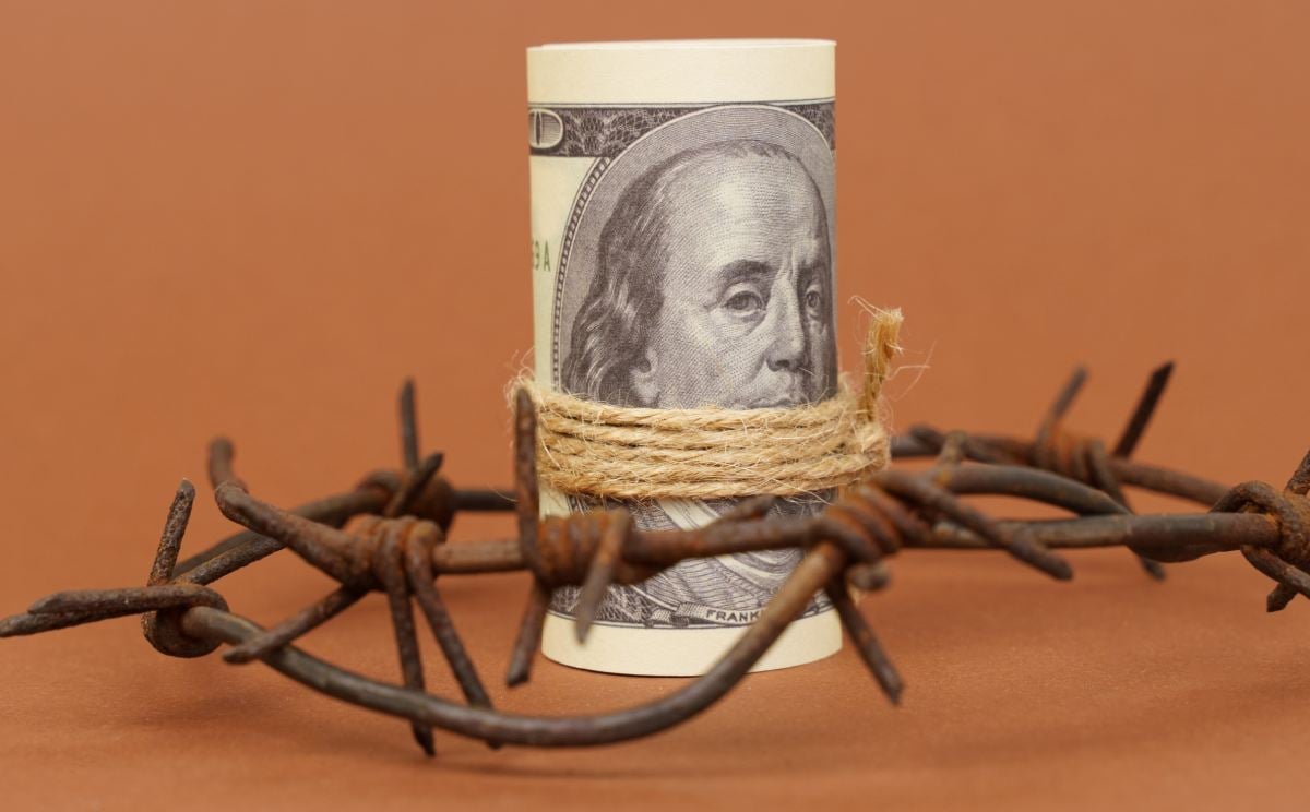 roll of dollar bills surrounded by barbed wire