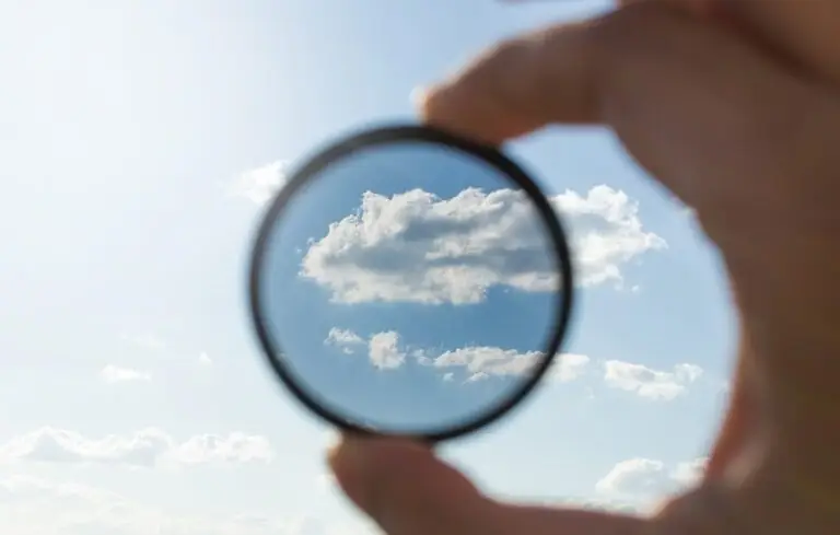 Hand holding a lens up to the sky, bringing clouds into focus
