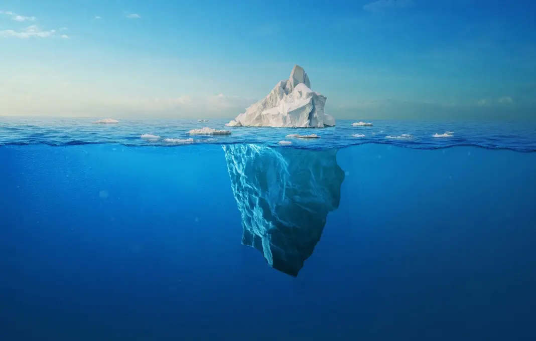 white iceberg floats in the ocean with a view underwater.