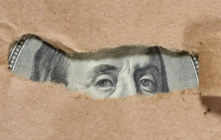 A piece of a hundred dollar bill is visible through a hole in the paper.